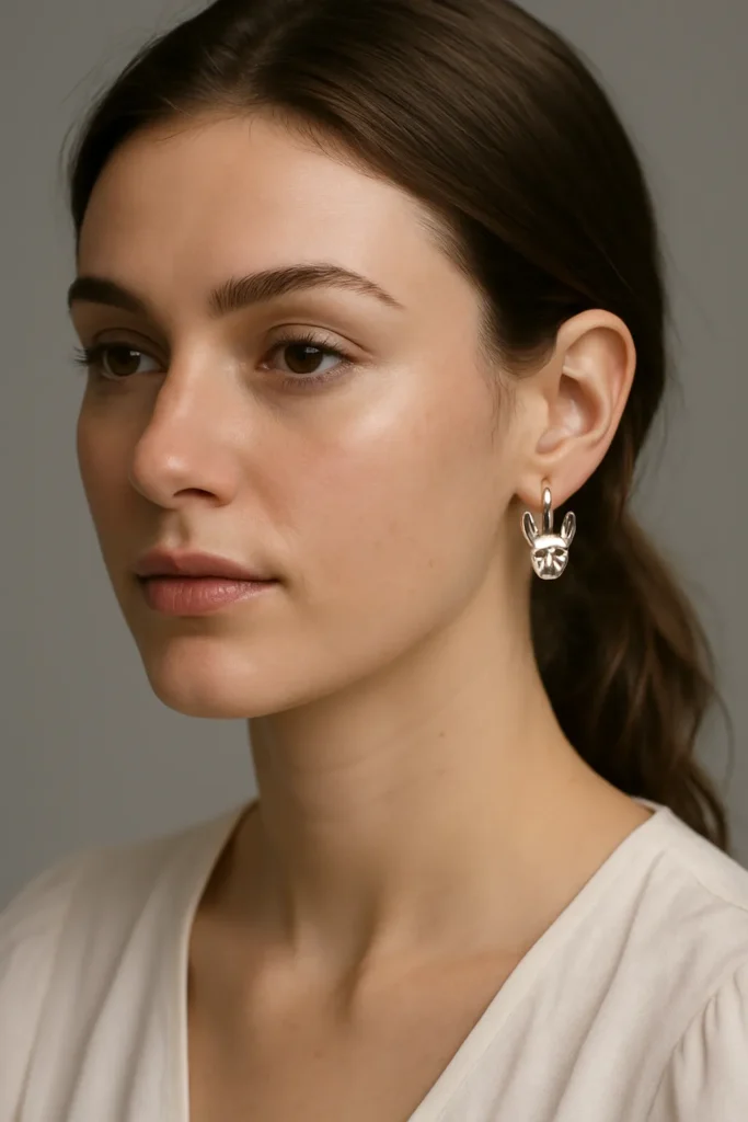 Close-up of woman wearing silver hoop earrings with sculpted animal head charm against neutral background.