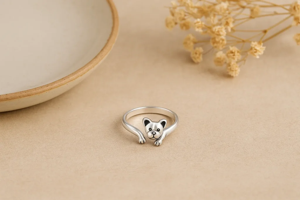 Elegant silver ring shaped like a dog with front paws wrapping around, styled on neutral background with dried flowers.